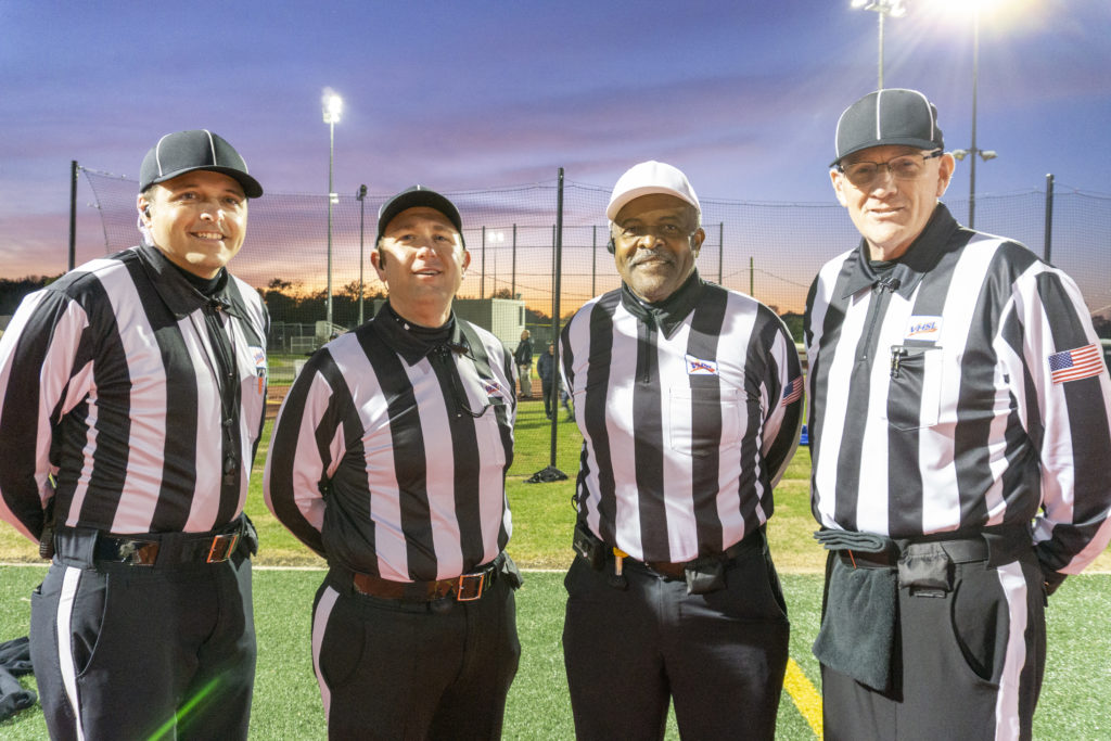 Four football officials posing for a photo under Friday Night lights